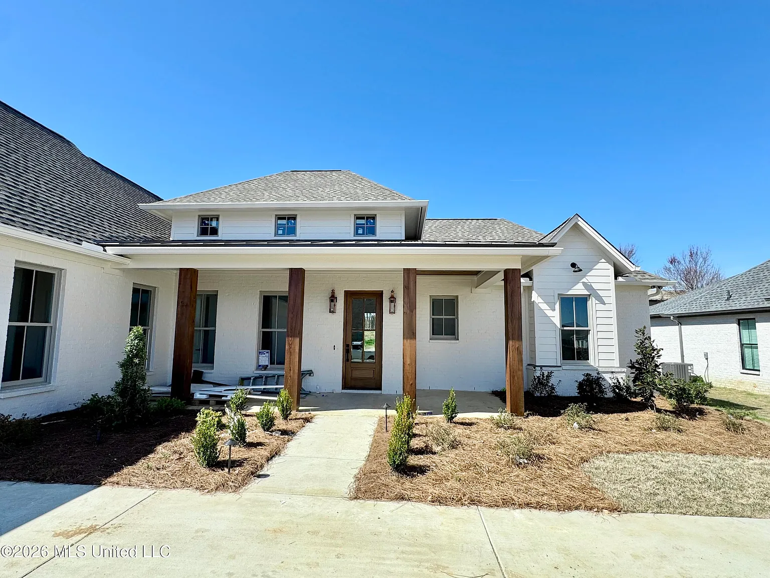 Front exterior of 115 Genoa Drive — a white-brick farmhouse with a covered front porch and cedar posts in the Fontanelle community of Madison, Mississippi.